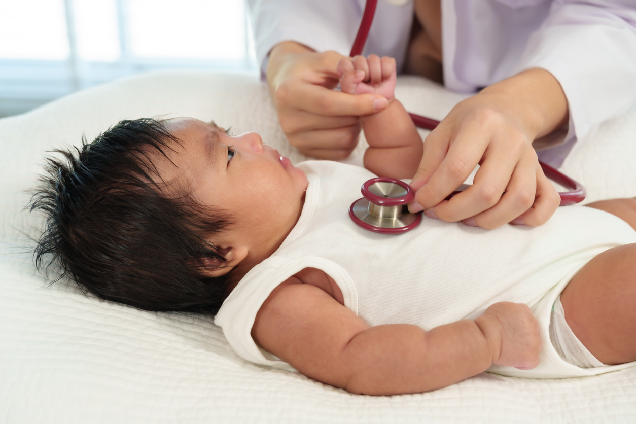 Newborn baby looking at pediatrician checking heartbeat with stethoscope
